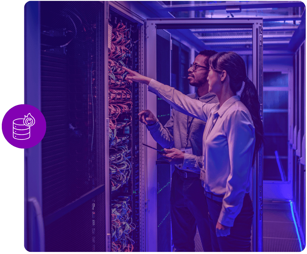 Dois técnicos num corredor de datacenter a inspecionar a cablagem de um bastidor.
