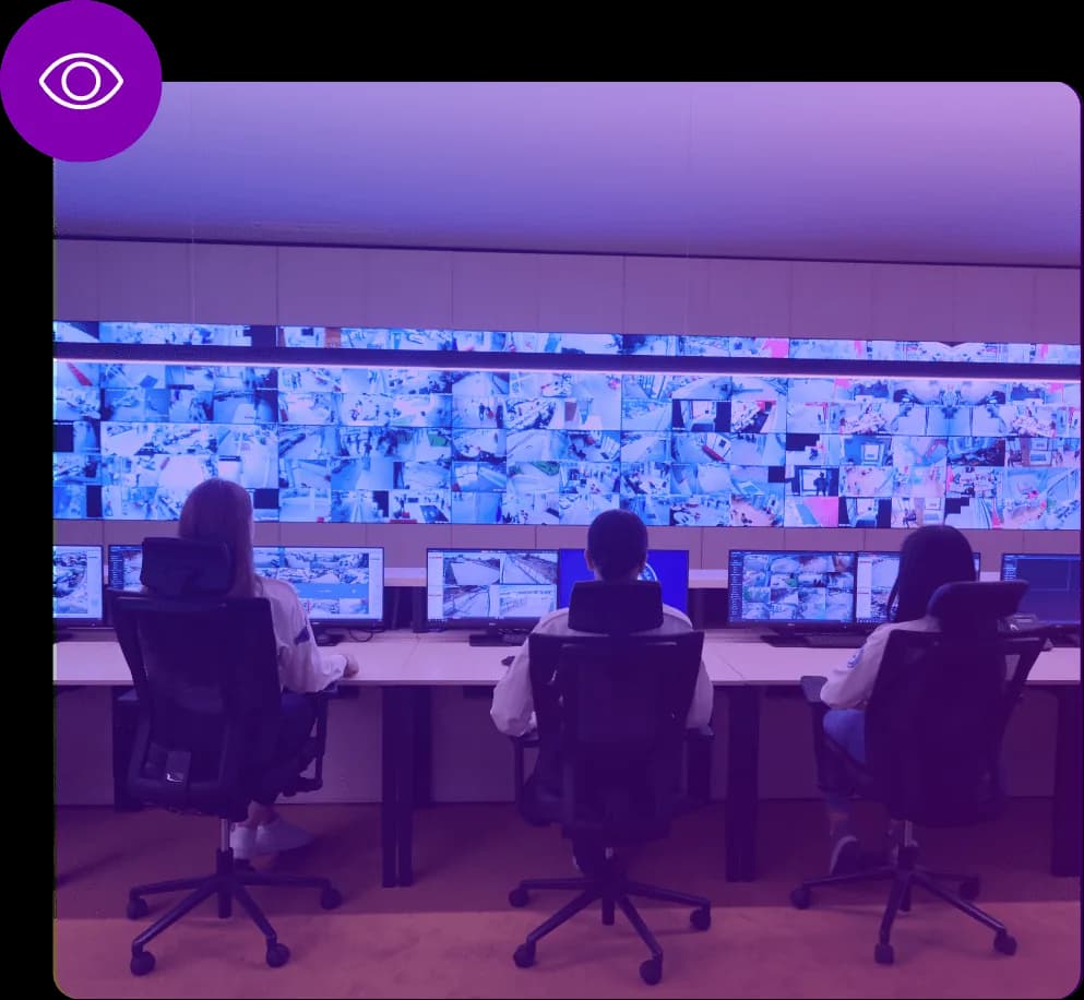 Três operadores numa sala de monitorização, de frente para uma parede de ecrãs com dezenas de câmaras em simultâneo.