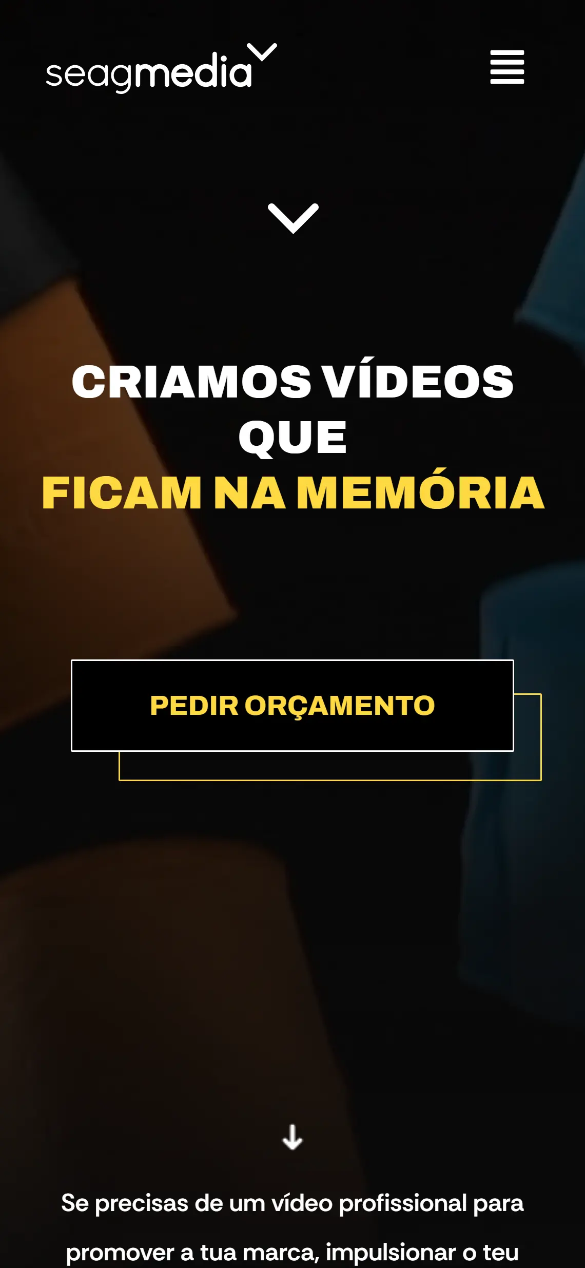 Página inicial da Seagmedia num telefone: logótipo, botão de menu, título em três linhas com a última a amarelo, botão de pedido de orçamento e, ao fundo, o início do parágrafo de apresentação, tudo sobre a fotografia desfocada de objectos coloridos.